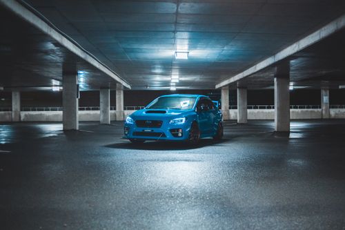 Free Contemporary design automobile driving on shiny floor in spacious parking building with glowing lamps on ceiling behind fence in evening Stock Photo