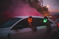 Unrecognizable men in glowing Halloween masks driving car at night