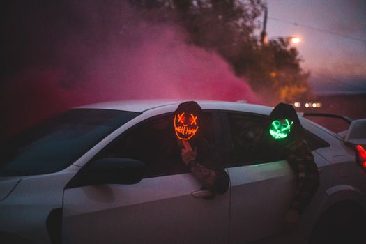 Unrecognizable men in glowing Halloween masks driving car at night