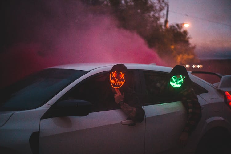 Unrecognizable Men In Glowing Halloween Masks Driving Car At Night