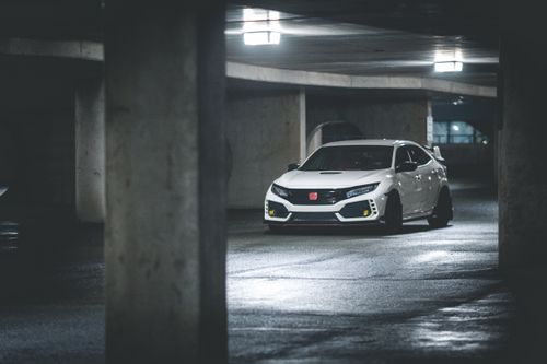 Free Contemporary white automobile driving on shiny floor illuminated by glowing ceiling lamps in car park with cement posts in evening Stock Photo