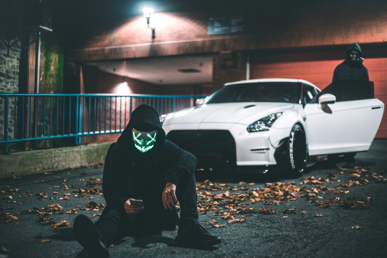 anonymous male in neon mask browsing internet on cellphone while sitti