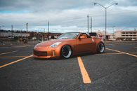 Side view of modern design orange automobile with convertible top on asphalt roadway with yellow marking lines behind buildings and lamp posts in town in daylight
