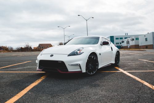 Free Contemporary style white automobile with shiny headlights on asphalt road with marking lines behind building and lamp posts in parking lot in town in sunlight Stock Photo