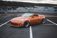 From above side view of modern style automobile with convertible top on asphalt pavement with marking lines in city parking lot behind cement fence and mountain with trees