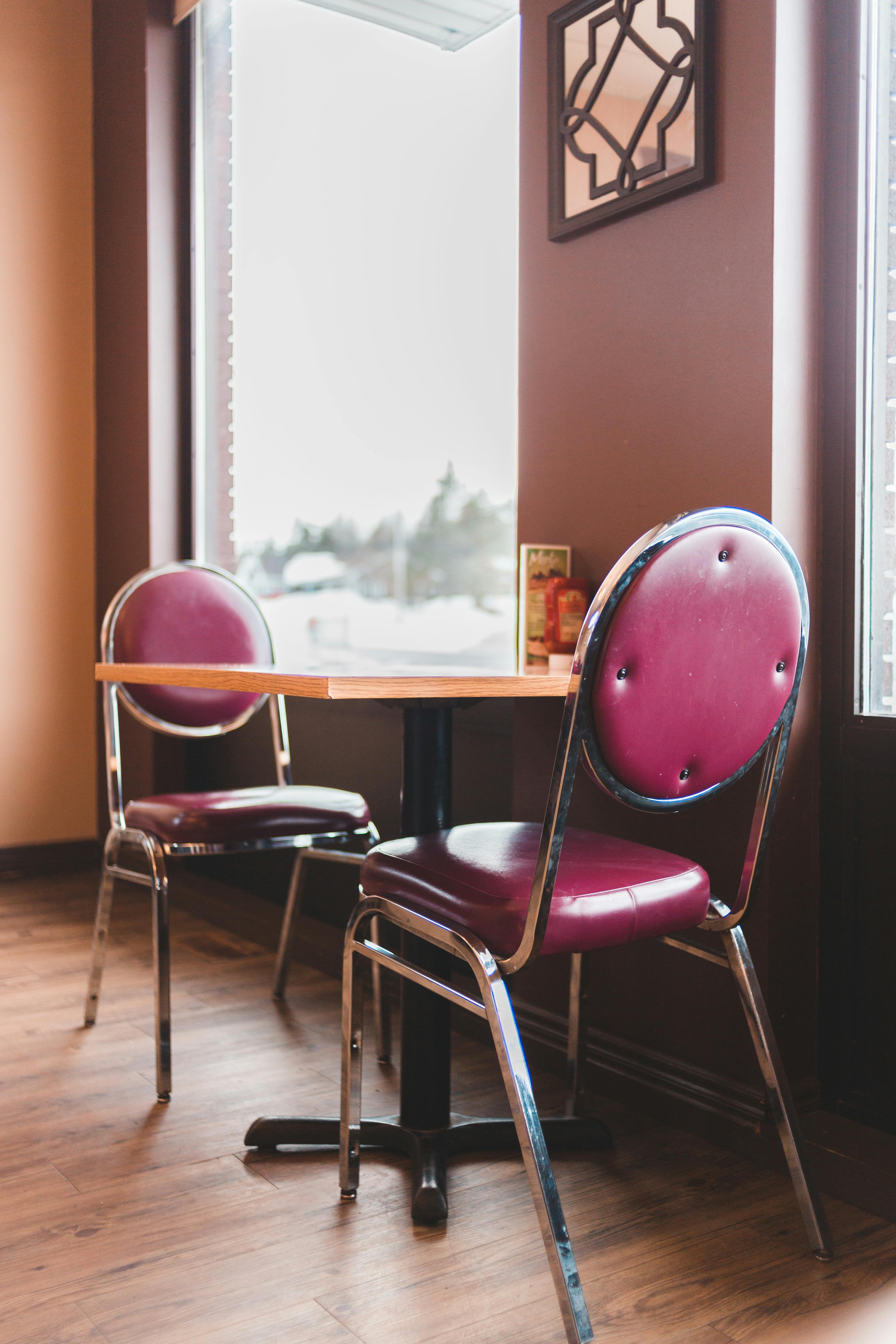 Free An inviting cafe interior featuring a table and two pink chairs by a large window. Stock Photo
