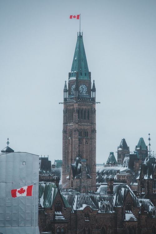 Free A low angle shot of the Peace Tower with snow and a Canada flag flying, highlighting Gothic architecture. Stock Photo