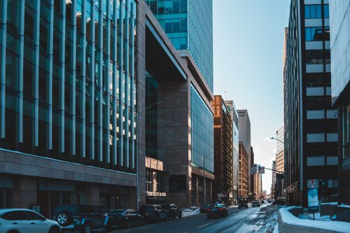 Free A bustling city street lined with modern skyscrapers and parked cars during daylight. Stock Photo