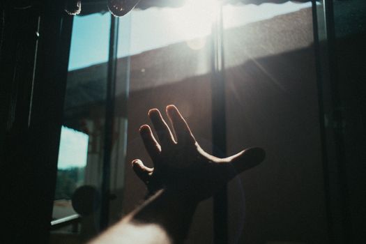 一只手伸向透过窗户洒入室内的明亮阳光