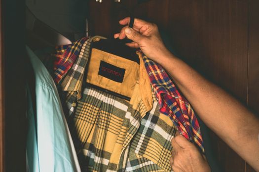 Adult holding a plaid Sportex shirt on a hanger in a wardrobe, showcasing casual menswear style.