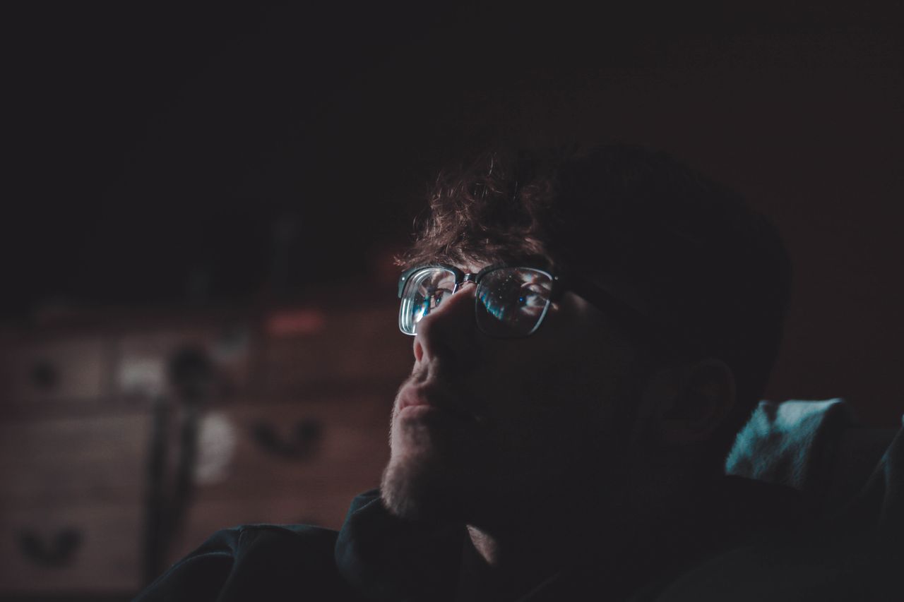 dark and reflective portrait of a man wearing eyeglasses in a dimly li