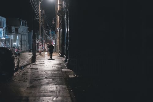 Free A lone person walking down a dimly lit city street at night, capturing urban solitude. Stock Photo