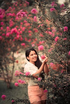 A happy woman admires pink flowers in a lush garden, enjoying nature's beauty.
