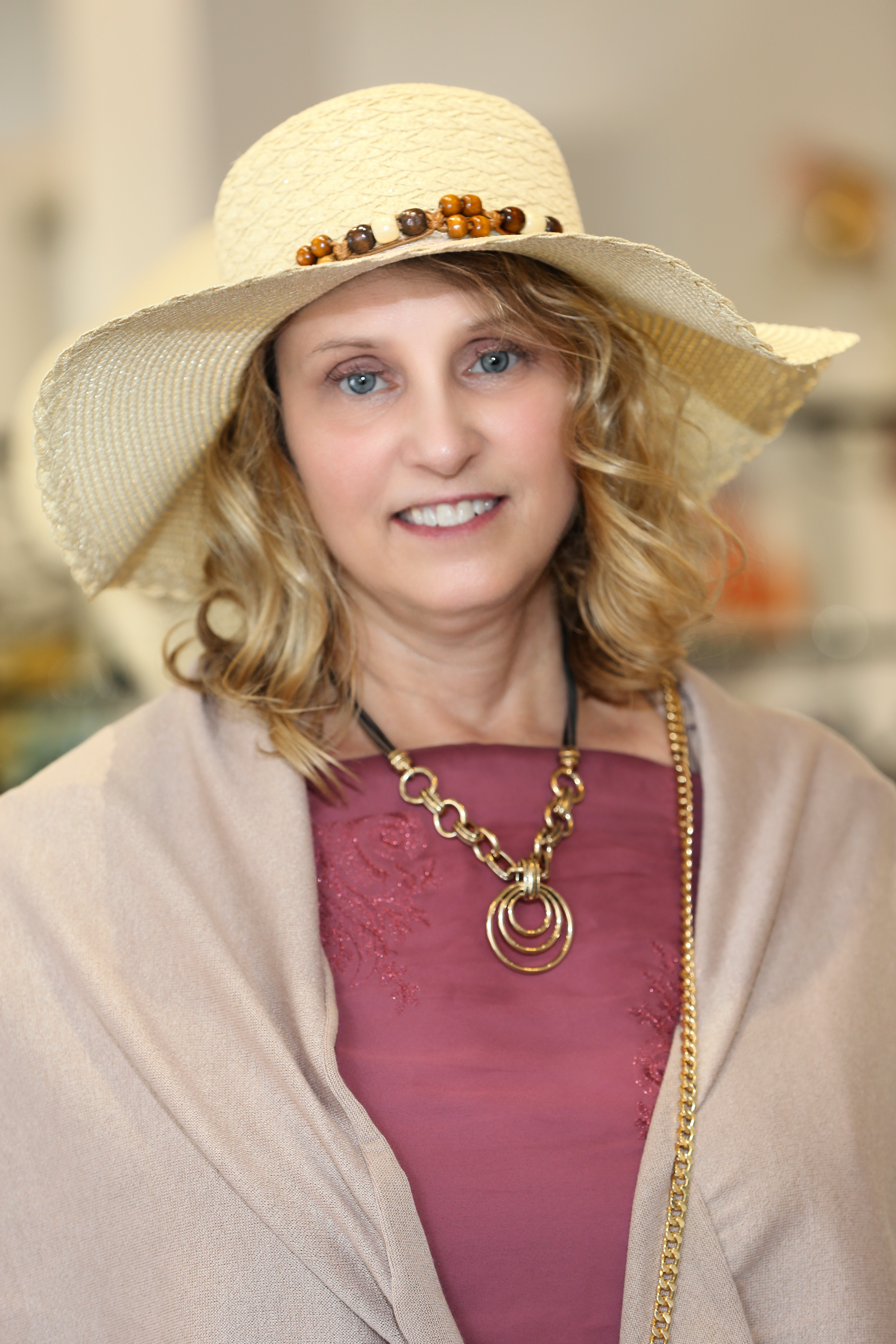 Woman wearing stylish straw hat and necklace, captured in a warm portrait indoors.