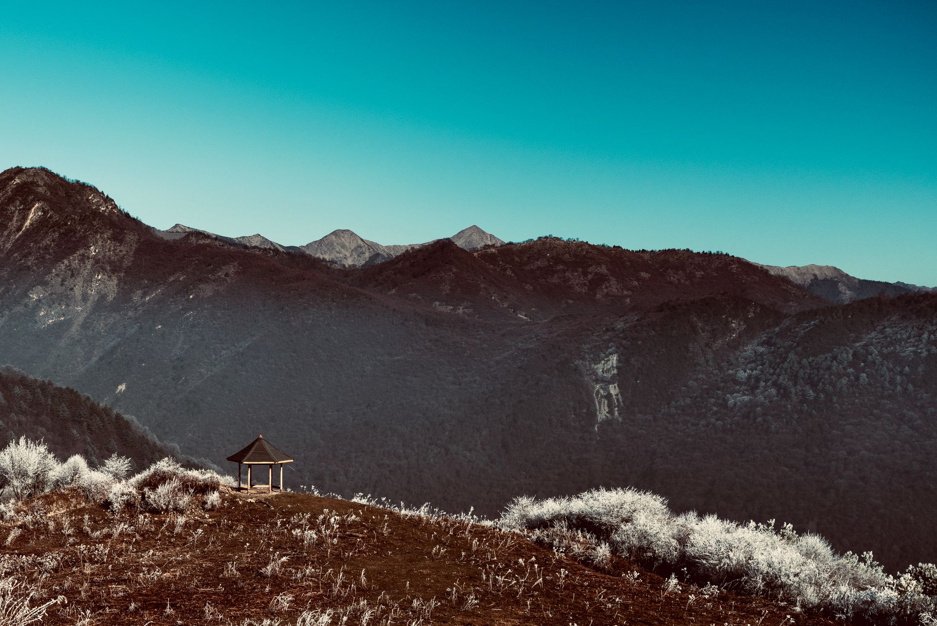 Scenic mountain view with a gazebo and frost on the grass under a clear blue sky.