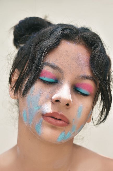 Young mindful ethnic female teenager with dirty face and makeup on closed eyes with tilted head on light background