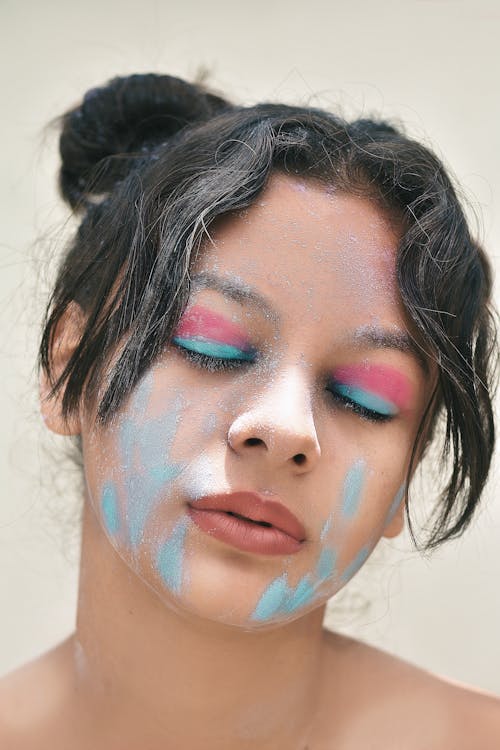 Young mindful ethnic female teenager with dirty face and makeup on closed eyes with tilted head on light background