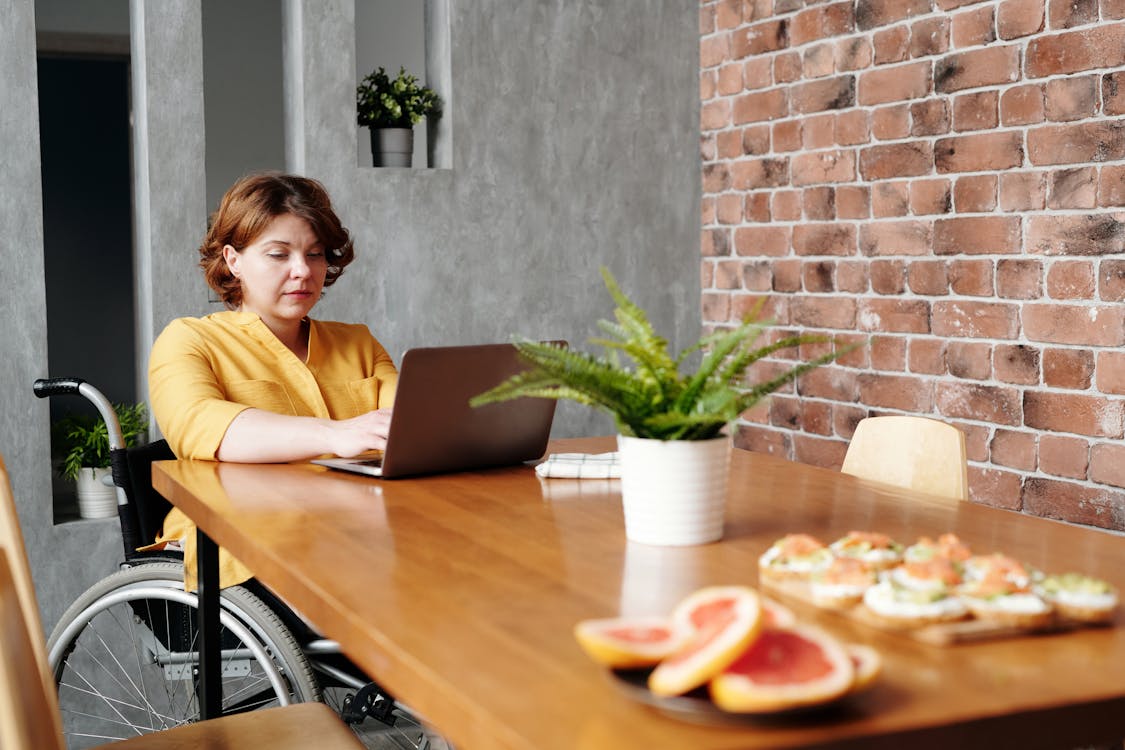 A woman using a laptop while seated in a wheelchair, demonstrating productivity and determination.