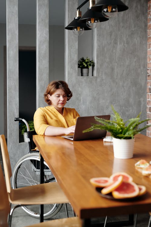 Free Woman in Yellow Long Sleeve Shirt Sitting on Chair in Front of Brown Wooden Table Stock Photo
