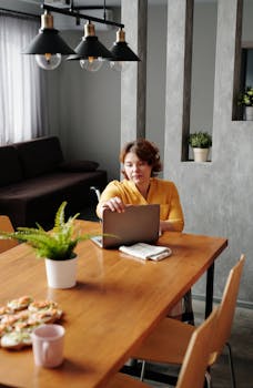 Woman working remotely from home, using laptop on a stylish dining table.