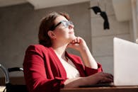 一位坐在轮椅上的女人，戴着眼镜，穿着红色西装，在明亮的咖啡馆里用笔记本电脑工作