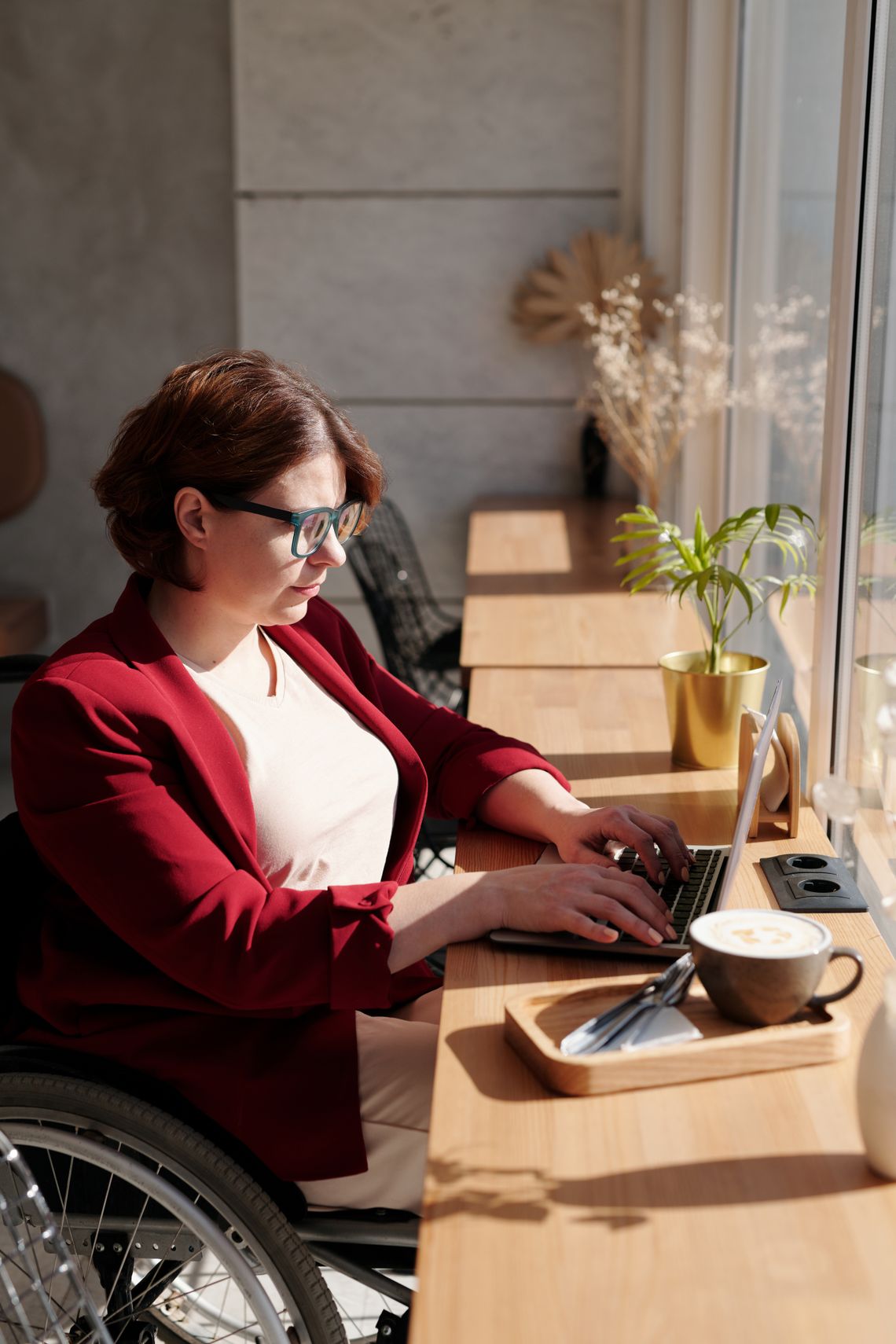Woman using a wheelchair while working on a laptop in a bright cafe