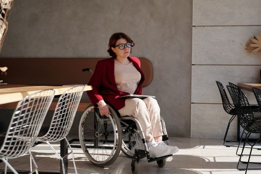 一位戴着眼镜、身穿红色西装外套的女士，坐在时尚的咖啡馆里的轮椅上
