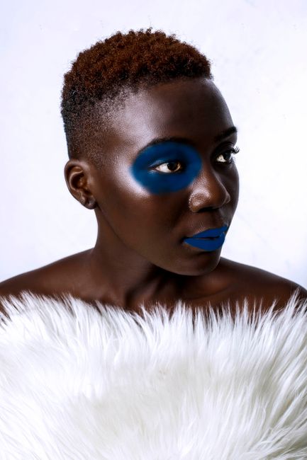 Striking portrait of a woman with unique blue makeup and afro hair in a fashion photoshoot.