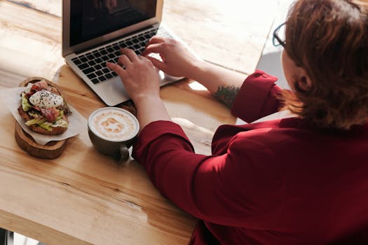 Businesswoman typing on laptop while enjoying coffee and breakfast at a café.
