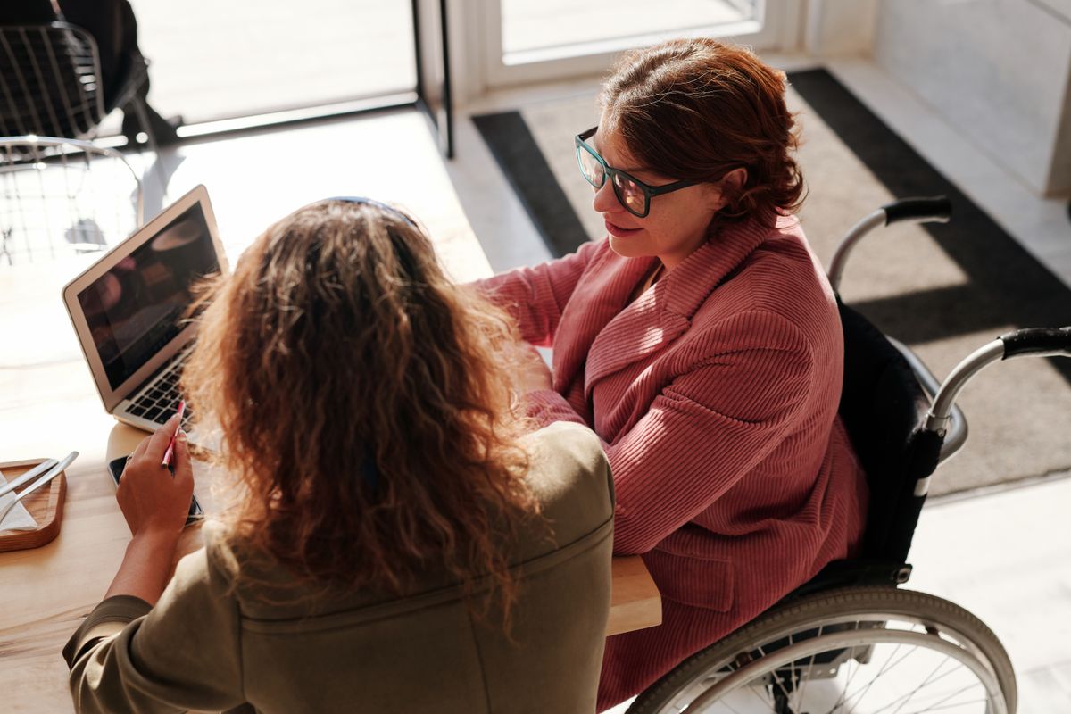 Two women working together at a laptop, including a wheelchair user