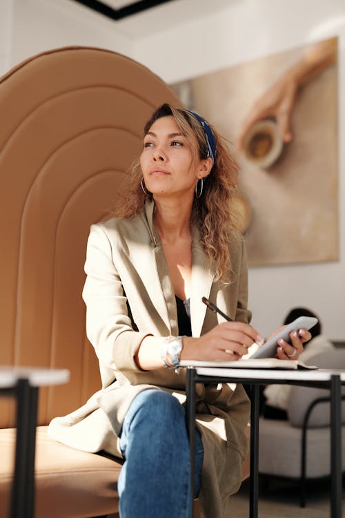Free Confident woman in blazer taking notes with pen and smartphone in cafe. Stock Photo