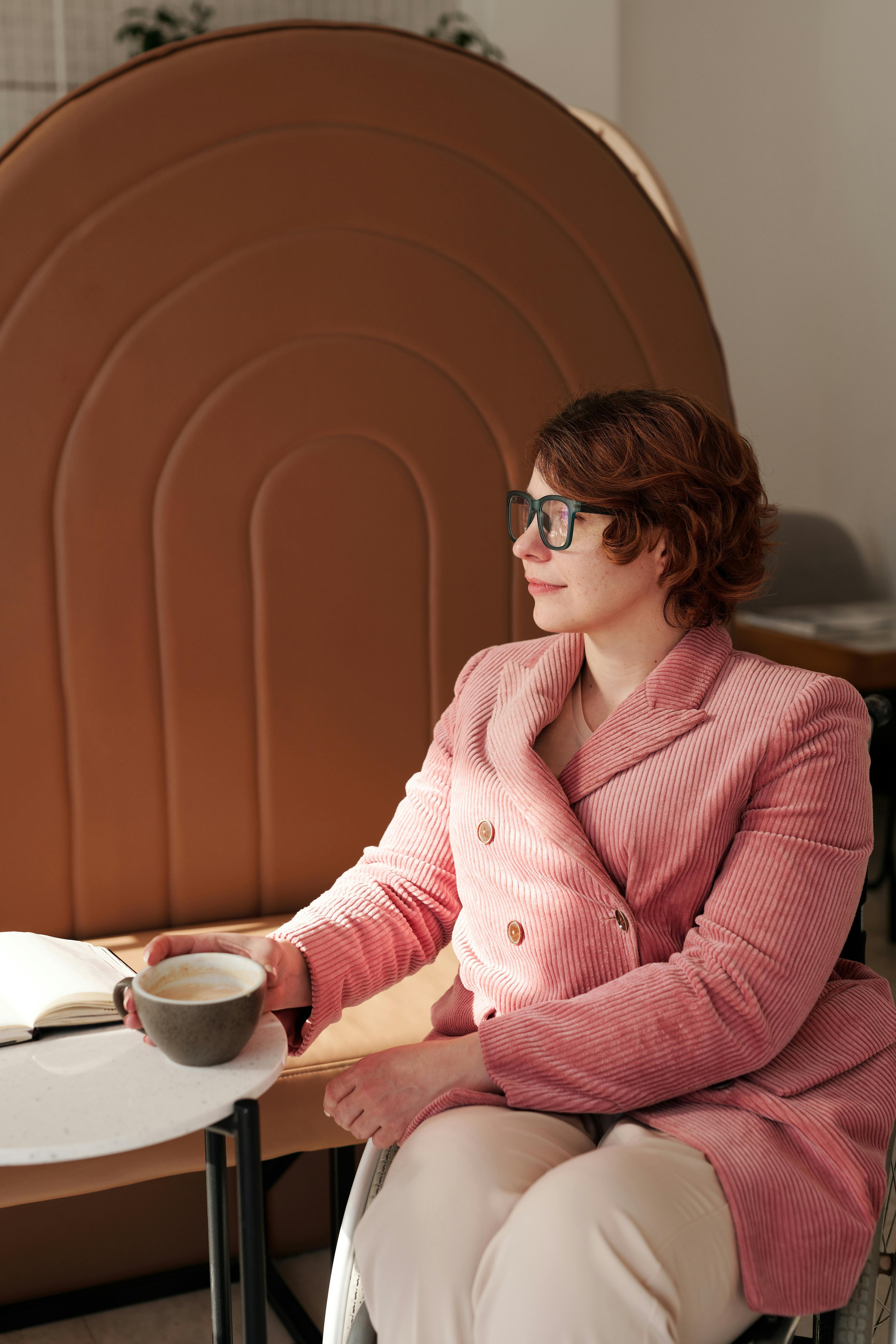 Businesswoman in pink blazer enjoying a coffee break indoors.