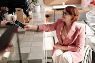 一位穿着粉红色西装外套的女商人在咖啡馆柜台用智能手机付款