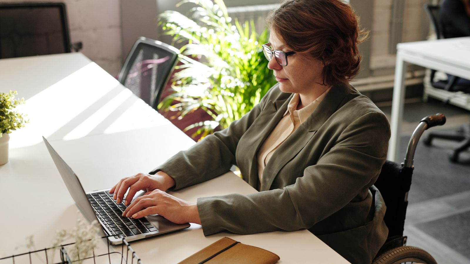 Businesswoman in wheelchair using laptop at office desk.