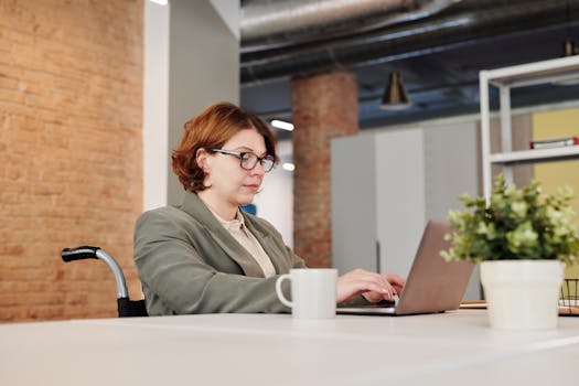 Professional woman in a wheelchair working on a laptop at a contemporary workspace.