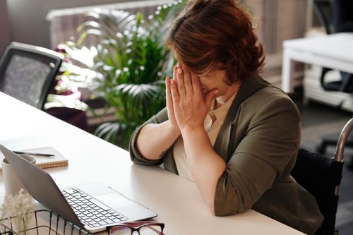 Free Businesswoman in wheelchair, tired at laptop, symbolizes office stress. Stock Photo