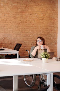 在现代办公环境中，一位坐在轮椅上的女商人正在办公桌前喝咖啡