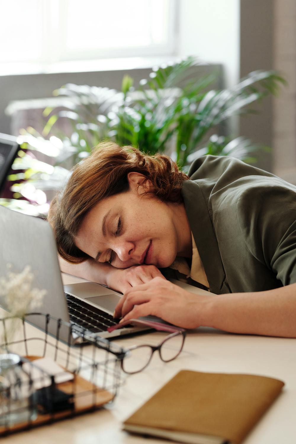woman asleep at her desk, on top of her laptop