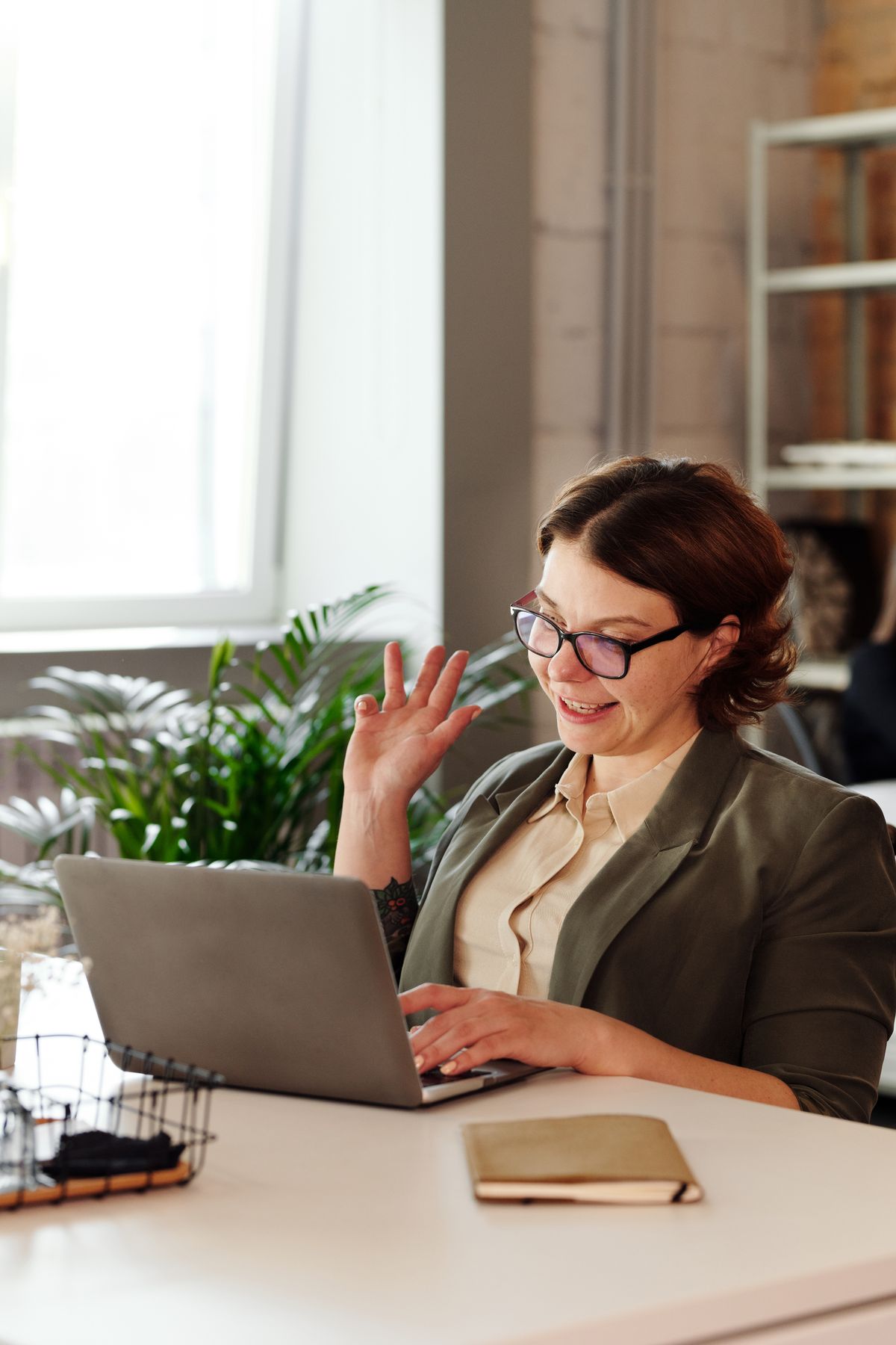 A small business owner smiling and waving at a colleague on her laptop screen