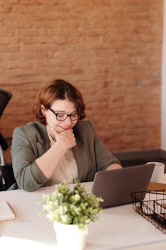 一位坐在轮椅上的女人在砖墙背景的家庭办公室里用笔记本电脑工作