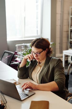 Businesswoman in a wheelchair working from home office on a laptop, focused on a phone call.