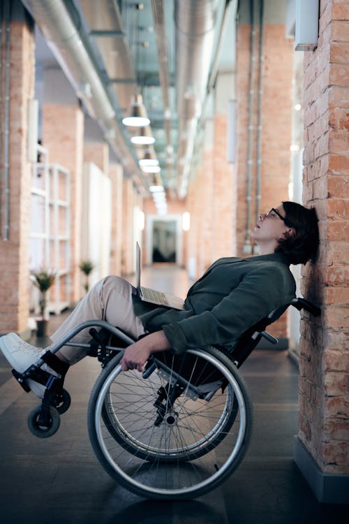 Free Woman Sitting on Wheelchair While Leaning on Wall Stock Photo