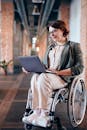 一位坐在轮椅上的女商人正在现代办公室里用笔记本电脑工作，面带微笑