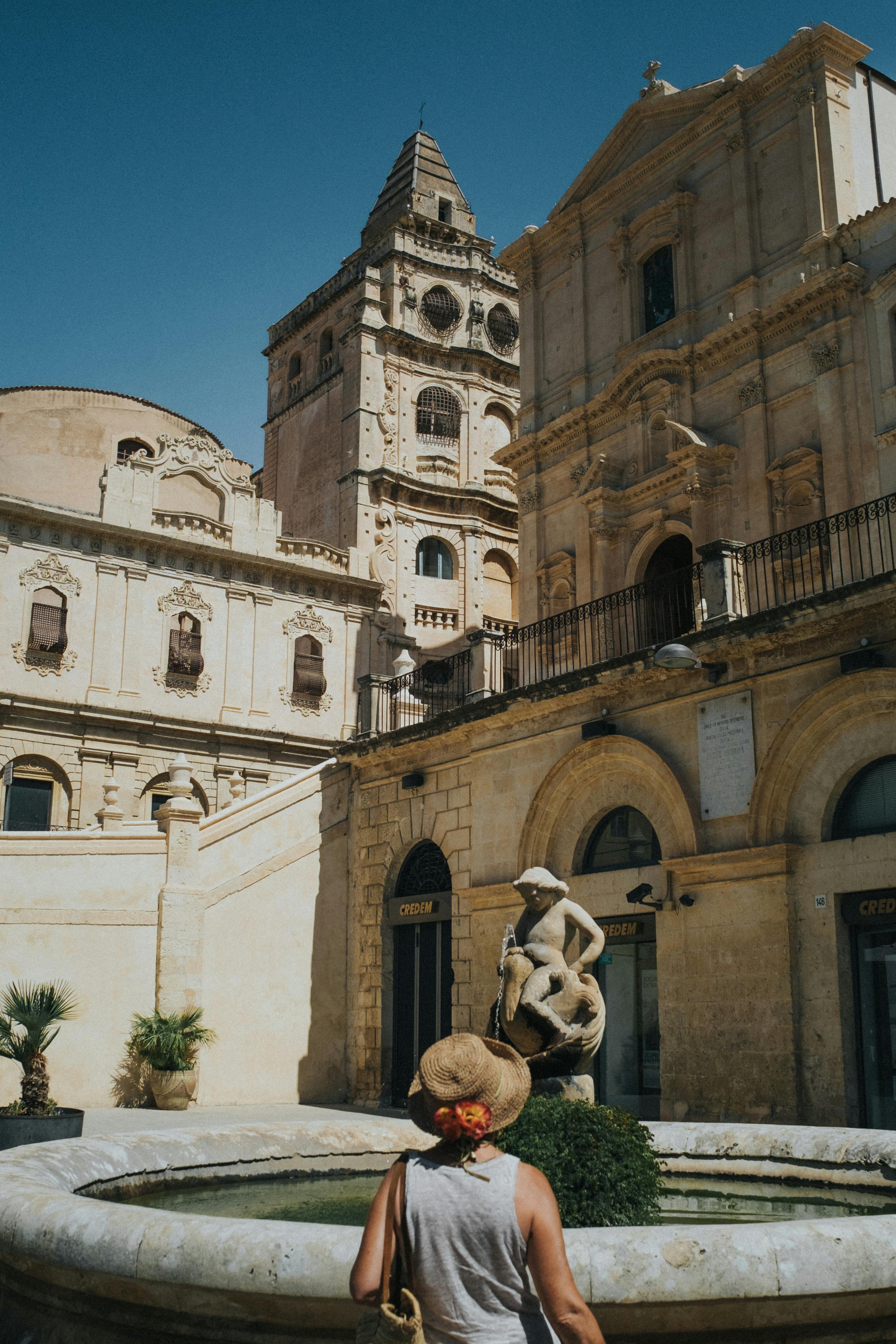 A woman admires the stunning baroque architecture of Noto, Sicily on a sunny day.