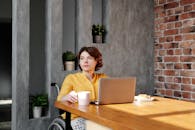 一位坐在轮椅上的女人在家用笔记本电脑工作，喝着咖啡