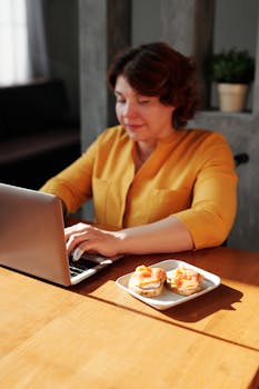 Woman working on a laptop at home during breakfast, embracing remote work lifestyle.