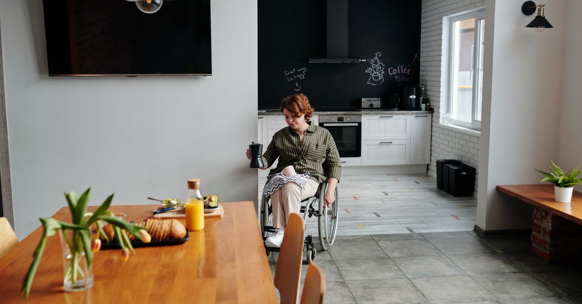A woman in a wheelchair holding coffee in a modern kitchen setting.