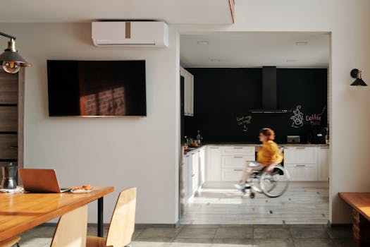 A woman in a wheelchair moves through a modern, stylish kitchen with white cabinets.