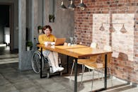 阳光满溢的室内，一位坐在轮椅上的女人正用笔记本电脑工作