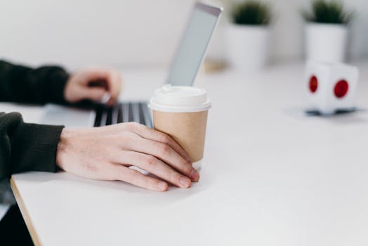 A person working at a clean, minimalist home office desk with a laptop and coffee cup.